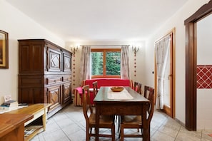 A dining area with a wooden table, chairs, a red tablecloth, and a window with curtains.