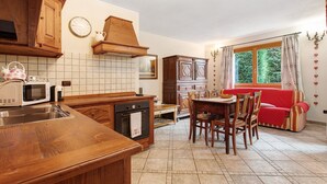 A kitchen with wooden cabinets, a microwave, a stove, and a dining area with a red sofa and chairs. - Apartment 'Bilocale 4' with Mountain View, Shared Terrace, and Wi-Fi (Gressan)