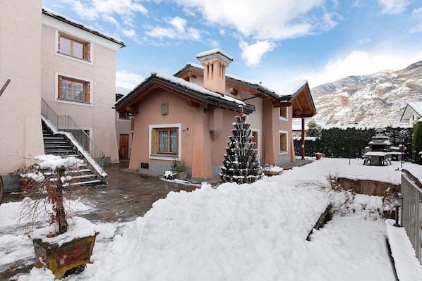 A two-story building with a staircase, a snow-covered roof, and a mountain backdrop.
