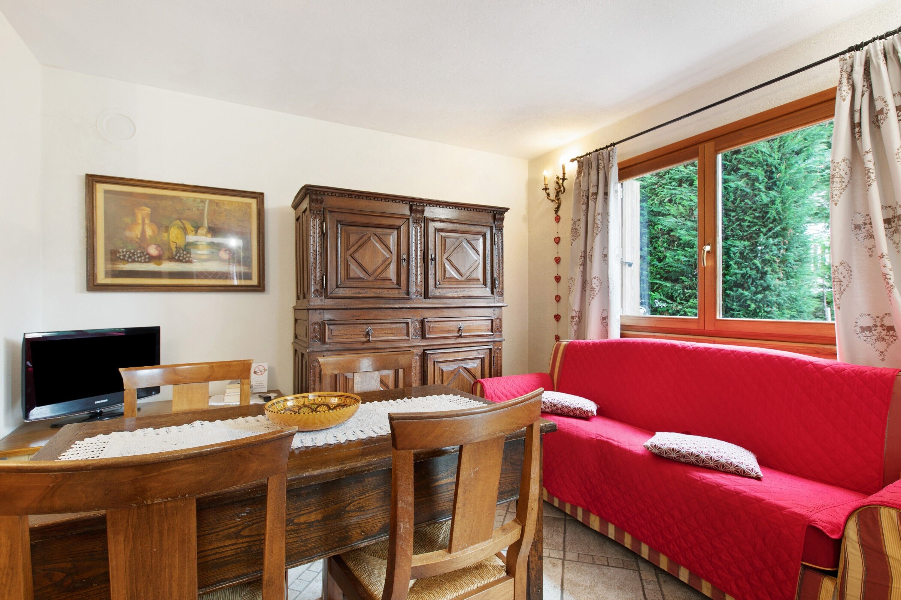 A dining area with a wooden table, chairs, a television, a cabinet, and a red sofa.