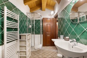 Un baño con ducha, lavamanos, espejo y puerta de madera.