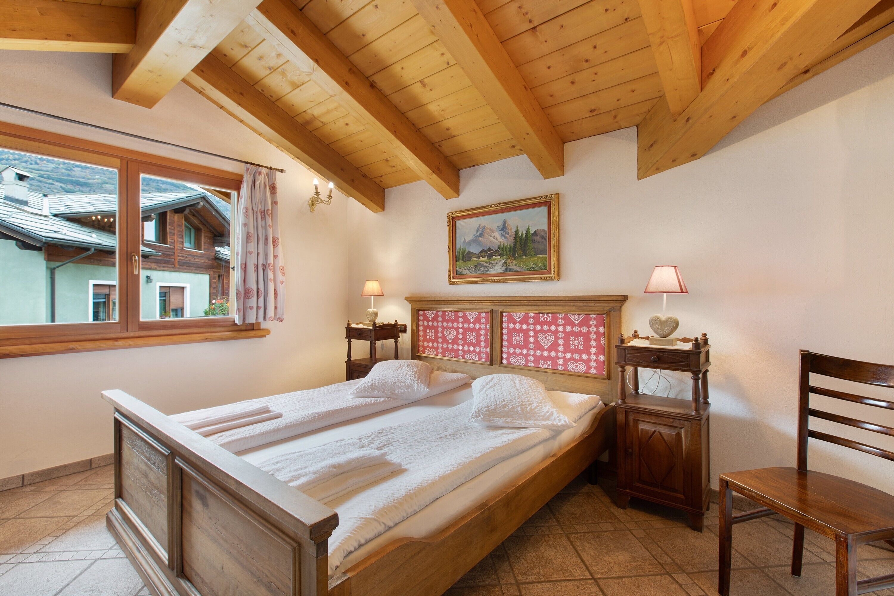 Ein Schlafzimmer mit einem Holzbett, einem Fenster mit Vorhängen, einem Bild an der Wand und einem Nachttisch mit einer Lampe.