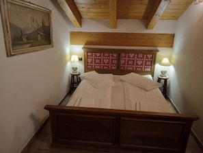 A bedroom with a wooden bed, two bedside lamps, a painting on the wall, and a red patterned headboard.