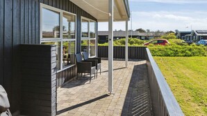 Un espace extérieur aménagé, abrité et doté d’une table et de chaises, situé à côté d’un bâtiment avec de grandes fenêtres.