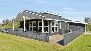 Une maison moderne dotée d’un patio couvert, de grandes fenêtres et d’une façade sombre.