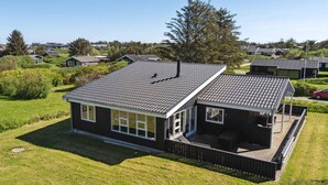 Une maison moderne dotée d’une grande terrasse, entourée d’une pelouse bien entretenue et d’arbres.