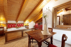 Un plafond en bois, un lit avec du linge de maison blanc, une table à manger avec des chaises et un grand miroir.