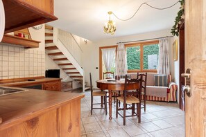 A kitchen with a wooden countertop, a dining table with chairs, a staircase, and a window with curtains.