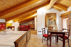 A bedroom with a wooden ceiling, a bed, a red sofa, a dining table with chairs, and a mirror.