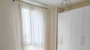 Une chambre à coucher comprenant un lit, une table de chevet, une armoire et un luminaire suspendu à motifs géométriques.