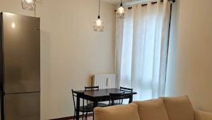 Un salon moderne avec un canapé beige, une table à manger avec des chaises, un réfrigérateur et des luminaires suspendus.