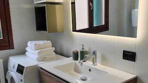 Une salle de bain moderne équipée d’un lave-linge intégré, d’un meuble-lavabo et d’un miroir.