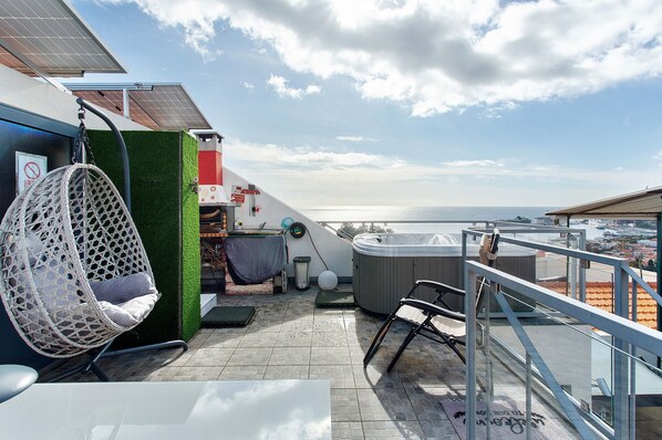A rooftop terrace with a hanging chair, a hot tub, and a view of the sea.