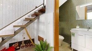 A staircase with wooden steps and metal railings, a white wall with a green textured section, a white sink with a green sign, and a potted plant. - Welcome to Your Home Away from Home with Sea View! (Funchal)