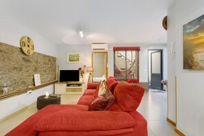 A modern living room with a red sofa, a flat-screen TV, a stone wall, and a painting.