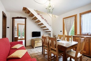 A dining area with a wooden table and chairs, a staircase with a railing, and a television on a wooden cabinet. - Apartment 'Trilocale 6' with Mountain View, Shared Terrace and Wi-Fi (Gressan)