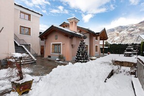 Un bâtiment à deux étages, doté d’un escalier, d’un toit enneigé et ayant une chaîne de montagnes en arrière-plan.