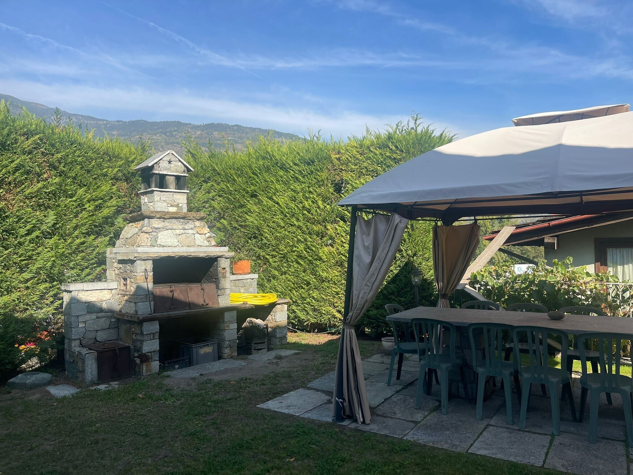 Un espace barbecue extérieur doté d’un grill en pierre, d’une table couverte avec des chaises et d’une tente.