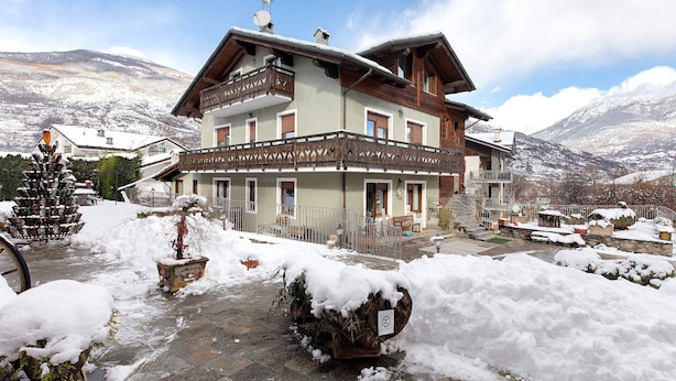 Un immeuble à plusieurs étages doté de balcons, un sol recouvert de neige et des montagnes en arrière-plan.