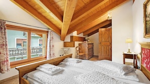 Une chambre avec un plafond en bois, un grand lit, une commode en bois et une fenêtre avec des rideaux.