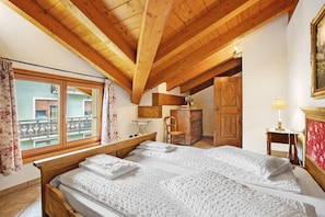 Une chambre avec un plafond en bois, un grand lit, une commode en bois et une fenêtre avec des rideaux.