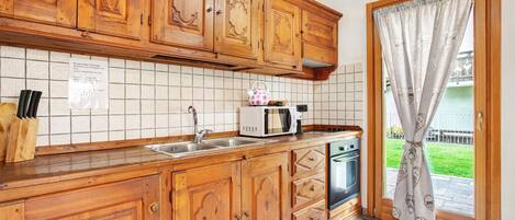 A kitchen with wooden cabinets, a microwave, a sink, and a window with a curtain.