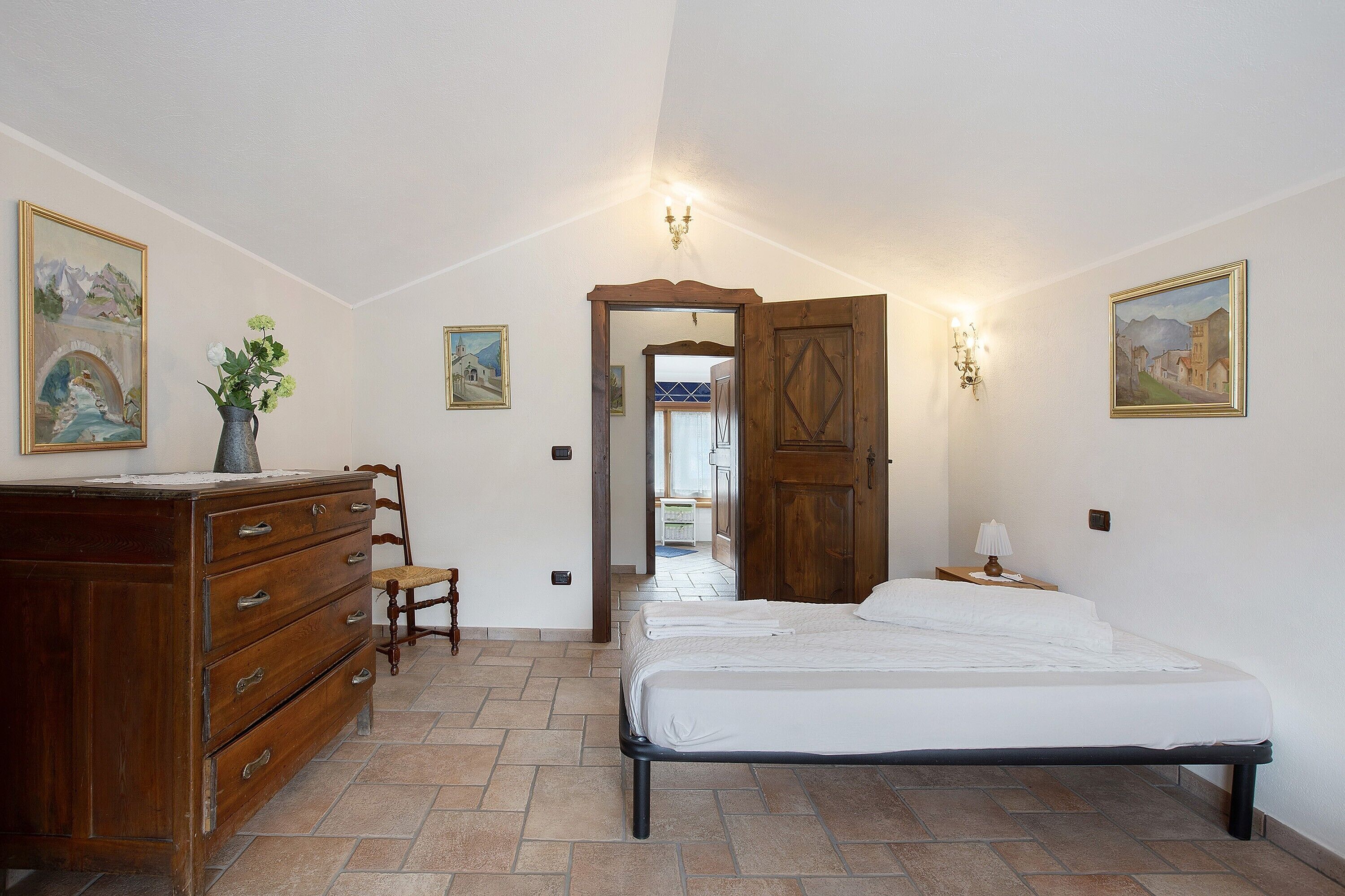 A bedroom with a bed, wooden dresser, and two wall-mounted lamps.