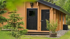 A wooden cabin with a black door and shutter, number 10, surrounded by greenery. - 4 Star Holiday Home in Glesborg (Glesborg)