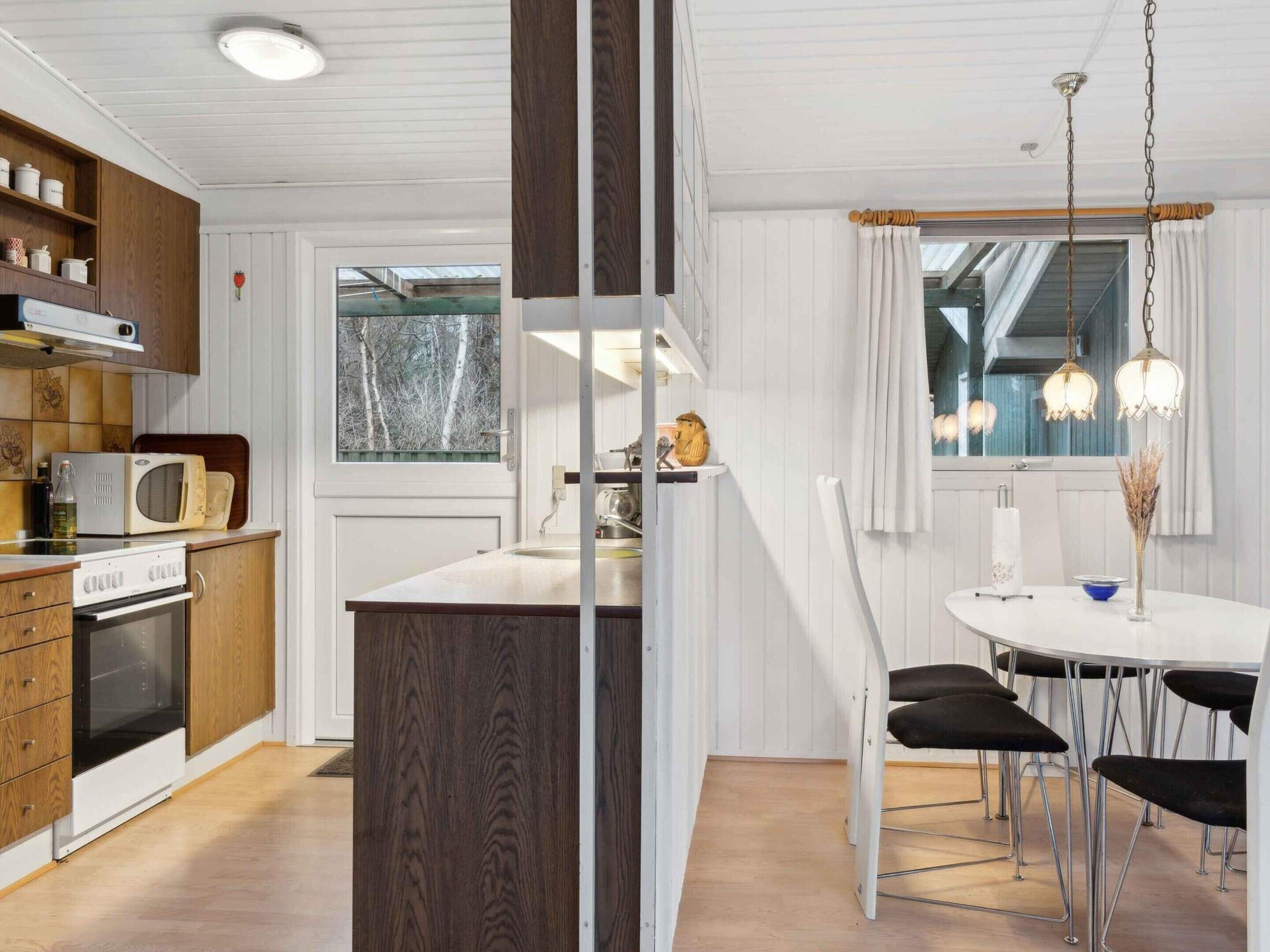A modern kitchen with wooden cabinets, a built-in oven, a microwave, and a dining area with a round table and black chairs.