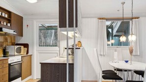 A modern kitchen with wooden cabinets, a built-in oven, a microwave, and a dining area with a round table and black chairs. - 5 Star Holiday Home in Saltum (Saltum)