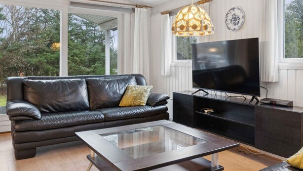 A modern living room with a leather sofa, a glass coffee table, and a flat-screen TV on a black stand. - 5 Star Holiday Home in Saltum (Saltum)