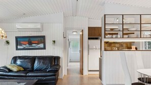 A modern living room with a black leather sofa, a glass coffee table, and a dining area with a white table and black chairs. - 5 Star Holiday Home in Saltum (Saltum)