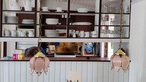 A kitchen with shelves holding dishes, cups, and a coffee maker. There are hanging lights and a window above the counter. - 5 Star Holiday Home in Saltum (Saltum)