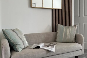 A grey sofa with two pillows, a magazine, and a pair of glasses on it.