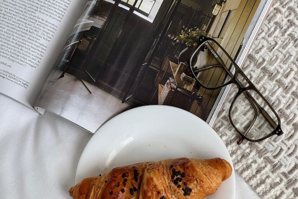 A book with a photograph of a building, a pair of glasses, and a plate with a croissant.