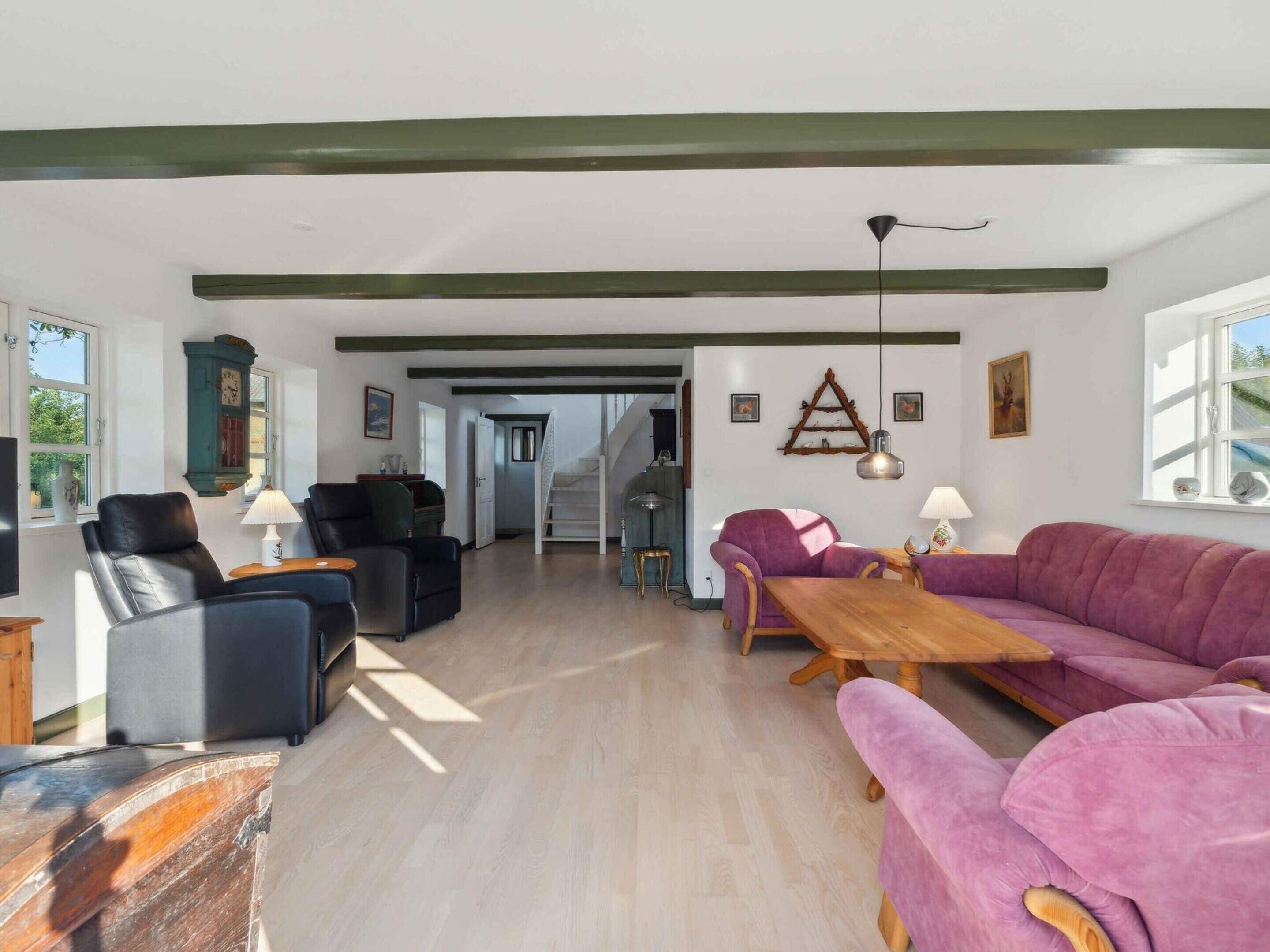 A spacious living room with a wooden dining table, a purple sofa, and a black leather chair.