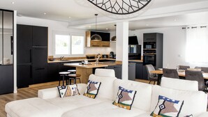 Una cocina moderna con armarios oscuros, una isla de madera y una zona de comedor con sofá y sillas blancos.