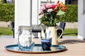 Ein Tisch mit einem Glasbehälter voller Zuckerwürfel, einer blauen Tasse mit Löffel und einer Blumenvase.