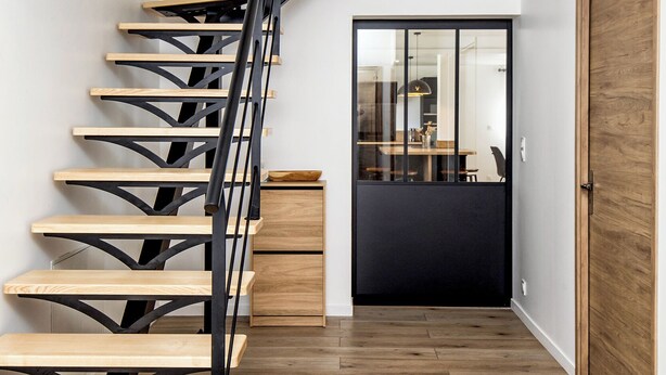 Una escalera moderna con escalones de madera y barandillas de metal negro que lleva a un piso superior.
