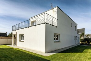 Ein modernes, zweistöckiges Haus mit Balkon, kleiner Veranda und gepflegtem Rasen.