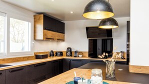 Una cocina moderna con armarios oscuros, encimera de madera y una isla grande. Se ve una cafetera, un tostador y un florero con plantas secas sobre la isla.