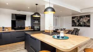 Una cocina moderna con una isla central, armarios negros, suelo de madera e iluminación colgante.