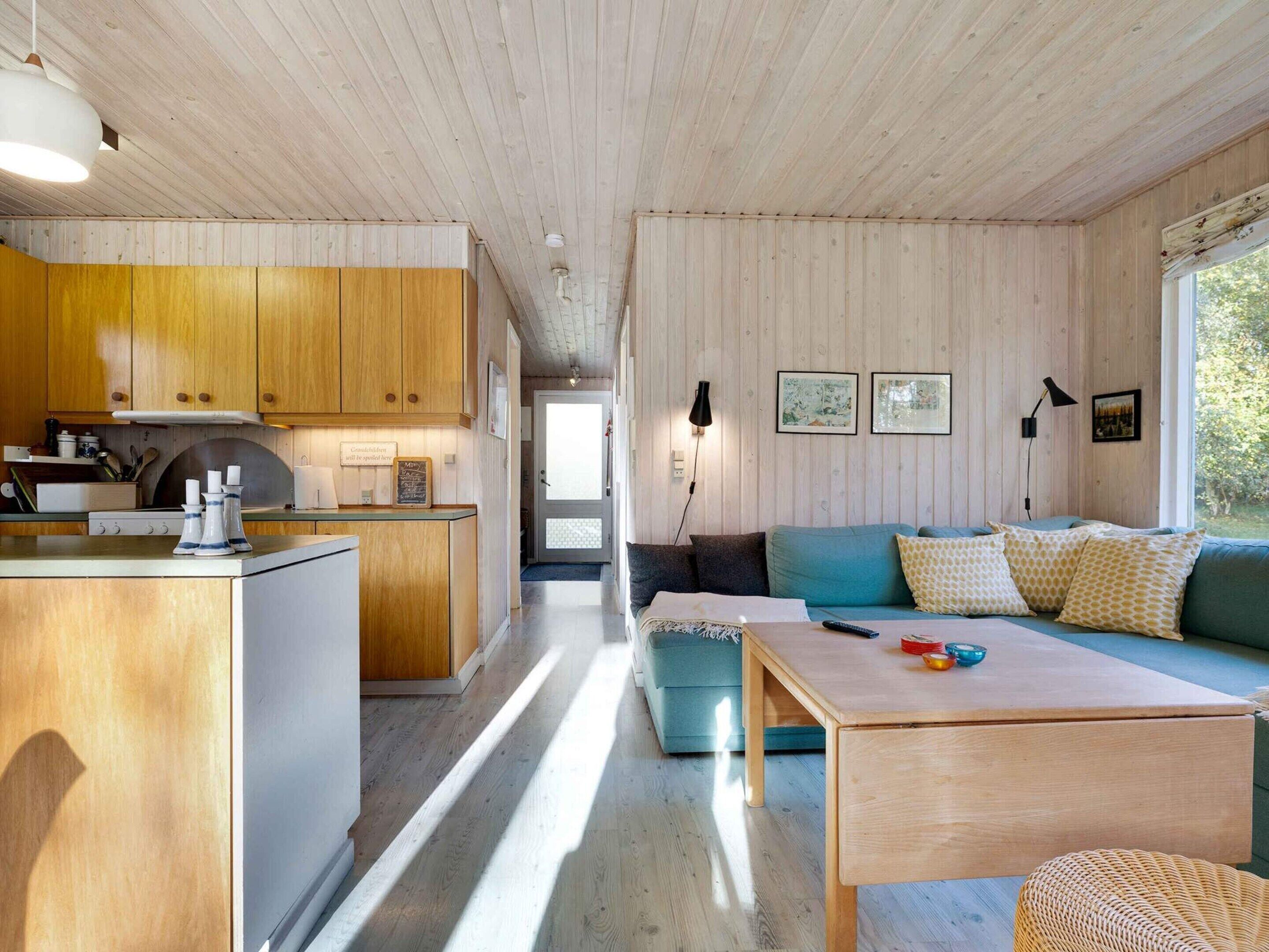 A modern interior with a kitchen, dining area, and living room, featuring wooden walls and a large window.