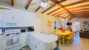 Una cocina con armarios blancos, microondas, estufa y un comedor con mesa y sillas amarillas.