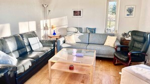 A modern living room with a leather sofa, a grey sofa, a glass coffee table, and a black office chair. - 5 Star Holiday Home in Faxe Ladeplads (Faxe Ladeplads)