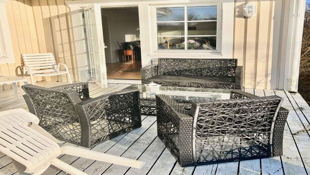 A covered outdoor seating area with wicker furniture and a white chair. - 5 Star Holiday Home in Faxe Ladeplads (Faxe Ladeplads)