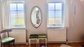 A room with two large windows, a mirror, a radiator, a wooden chair, and a bench. - 5 Star Holiday Home in Faxe Ladeplads (Faxe Ladeplads)