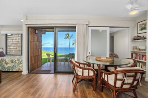 A room with a glass door leading to a balcony with a view of the ocean and palm trees. - Remodeled Ground Floor Ocean Views at Sealodge J5 (Princeville)