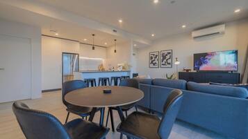 Una sala de estar moderna con una mesa de comedor redonda, sofá azul y televisor en la pared.