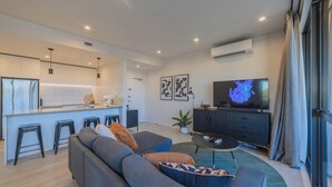 A modern living room with a sofa, a dining area with stools, a TV, and a kitchen in the background. - Cityside Comfort!  Modern 2BR, 2BA with Parking (Christchurch)